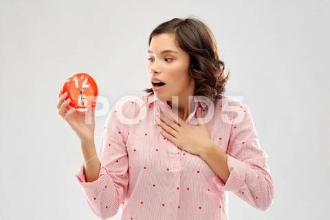 Shocked young woman in pajama with alarm clock Stock Photos