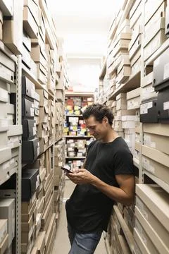 Shoe store assistant in storeroom with using smartphone Stock Photos