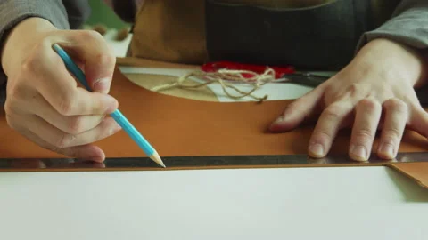 A shoemaker draws a line with a pencil on a large piece of genuine leather to Stock Footage 143722494