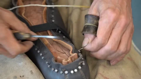 Shoemaker hand stitching the welt of a leather boot with yellow waxed thread 動画素材 346303144