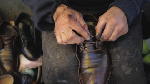 Shoemaker hands insert laces to leather boots at shoe manufacturing workshop Stock Footage 219285948