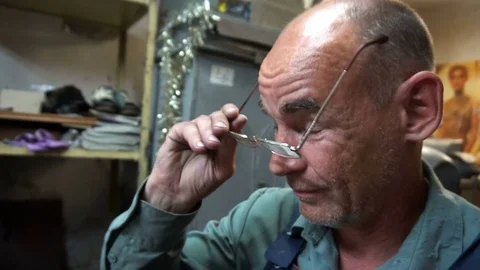 The shoemaker puts on his glasses and starts its work Stockbeeldmateriaal 77869394
