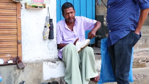 A shoemaker sits on the pavement, sewing a shoe. Stock Footage 246079251