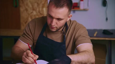 Shoemaker sketching a new design on a notebook Stock Footage 308932398
