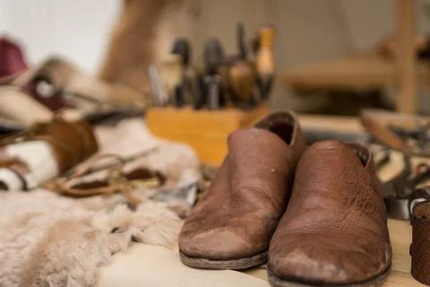 Shoemaker working desk with focus on ready shoes foreground and set of tools Stock Photos