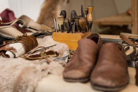 Shoemaker working desk with set of tools, ready shoes foreground and material Stock Photos