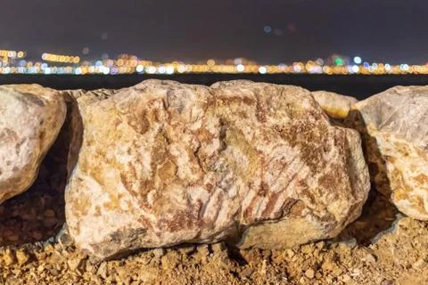 A shoot with far city lights behind sea and focus on white rocks Stock Photos