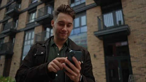 Shooting from below of cheerful young man smiling using smartphone standing in Stock Footage 297630383