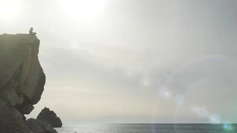 Shooting from below a man sitting on the edge of a cliff near the shore. The Stock Footage 131294814