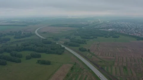 Shooting from a drone flying over a road among fields. . Video stock 333514476