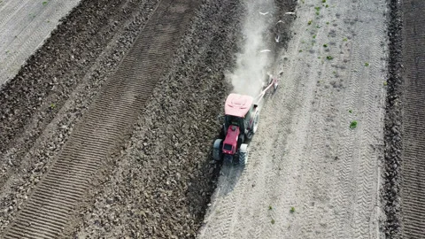 Shooting from drone flying over tractor on cultivated farm field Stock Footage 220120882