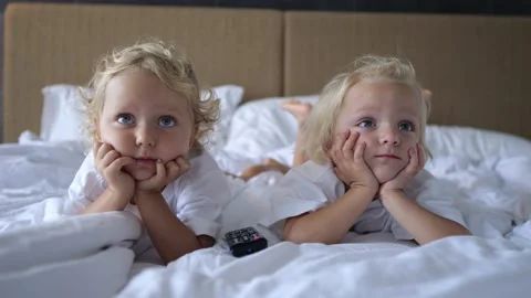 Shooting sisters from the foreground close-up. They lie on the bed and watch TV Stock Footage 220106511