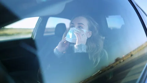Shooting through side window of confident young woman putting on Covid-19 face Stock Footage 148753634