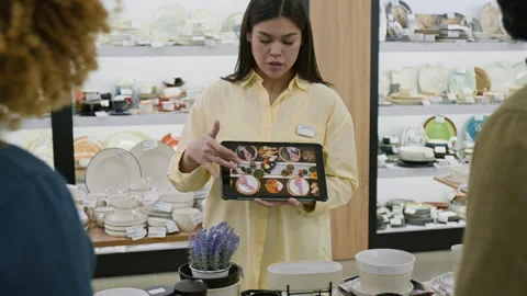 Shop Assistant Presenting Dinnerware Photos on Tablet to Customers Stock Footage 321776235