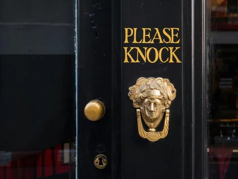 Shop door with a please knock text sign and ornamental brass door knocker. Stock Photos