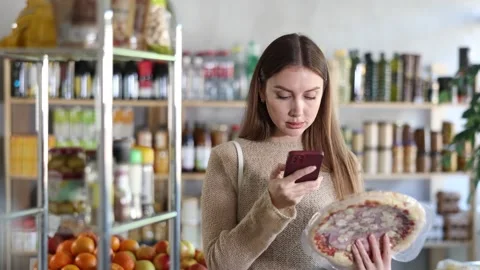 In shop girl scans QR code and take reading on pizza with prosciutto filling Stock Footage 309522623