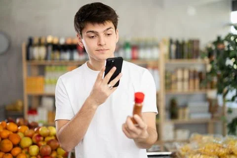 In shop guy scans QR code and take reading chopped red ground pepper using phone Stock-Fotos