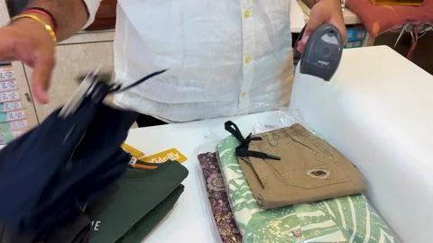 Shop worker scanning barcode on folded clothes with handheld scanner at retail Stock Footage 332913097