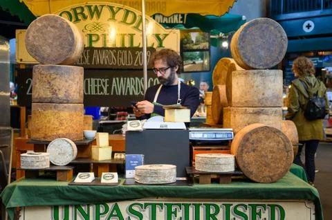 Shopkeeper using a smartphone while waiting for customers at a cheese market  Stock Photos