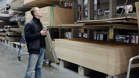 Shopper comparing different types of wood using a smartphone in the lumber aisle Stock Photos