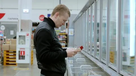 Shopper examines product labels while comparing various frozen food options in Stock Photos