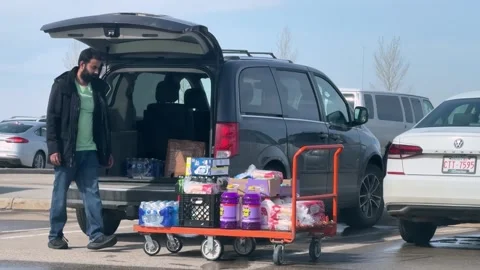 A shopper loads crates of bulk goods into a van, in a Costco parking lot. Stock-Footage 333424127