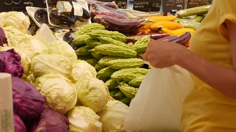 The shopper places a bitter melon into a plastic bag. The scene captures a Vídeo Stock 313485492