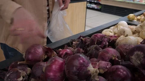 A shopper selects a red onion in a store and places it in a bag. 스톡 동영상 311588272