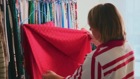 Shopper studies vivid red cloth among varied fabrics Stock Footage 333749878