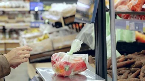 Shopper using a digital scale to weigh fresh bell peppers in a supermarket Foto stock