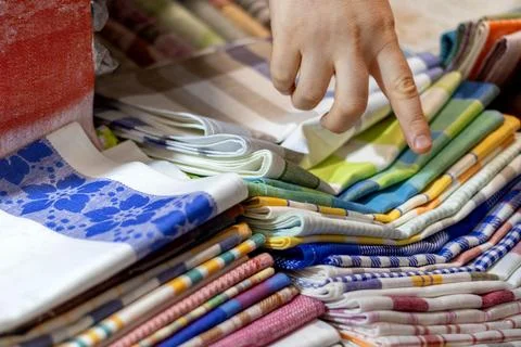Shopper's hand points to selected item in colorful stack of folded fabrics .. Stock Photos