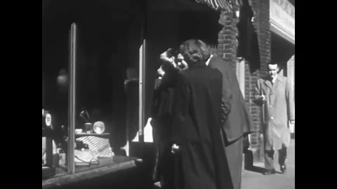 Shoppers look at a display in the window of a store and a public speaker motions Stock Footage 88555362