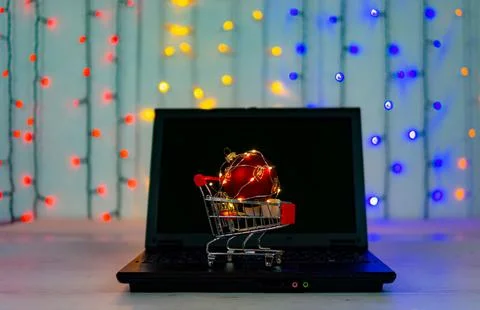 Shopping cart with big christmas ball and garlands on the keyboard of laptop. Stock Photos