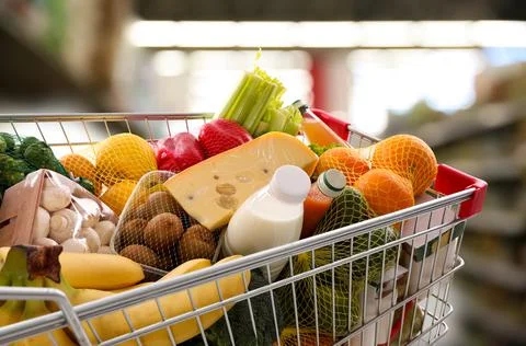 Shopping cart with different groceries in supermarket Stock Photos