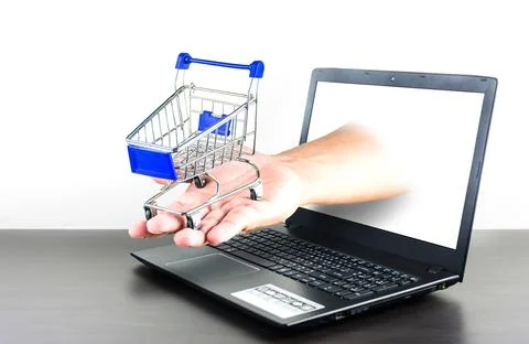 Shopping cart in hand with Computer notebook blank screen on wood table 스톡 사진