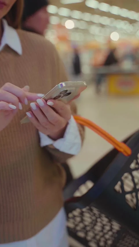 Shopping for groceries while checking a shopping list on a smartphone in a busy 스톡 동영상 293674424