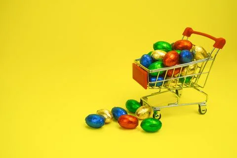 Shopping trolley filled with multi-colored candies on a yellow background Stock Photos