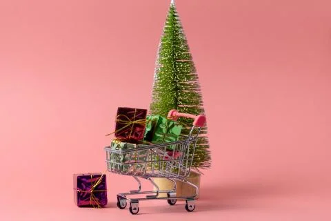 Shopping trolley full of present boxes against christmas tree on a pink backg Stock Photos