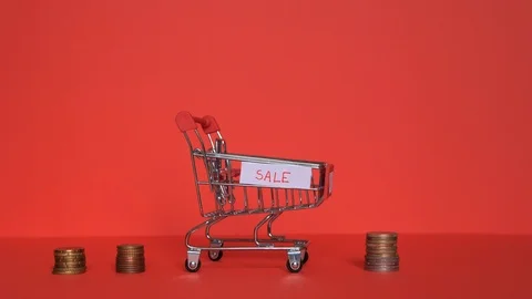 Shopping trolley with gift boxes and coins next to it in the red background. Video stock 120085494