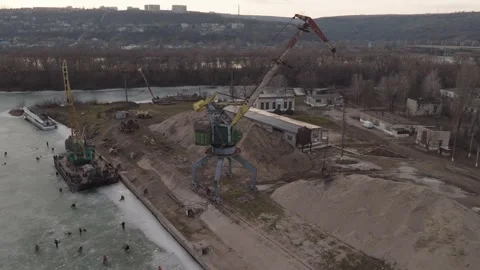 Shore-based rail-mounted portal crane beside aggregate stockpiles in a drone Stock Footage 345368933