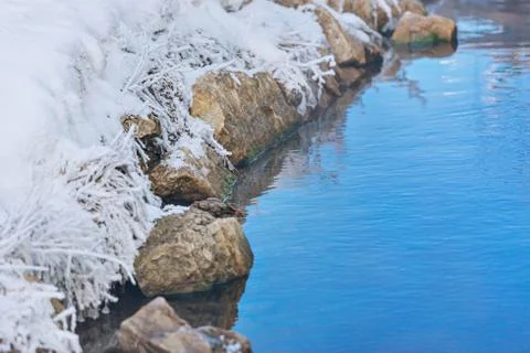 The shore is covered in frost on a frosty day. unfrozen water and snow on roc Stock Photos