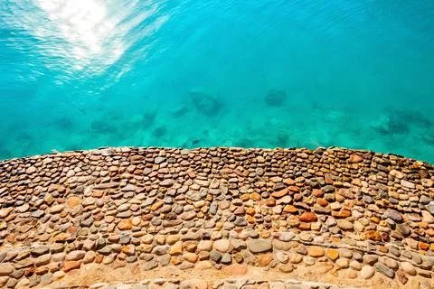 Shore is made of stone with blue clear water. Stock Photos