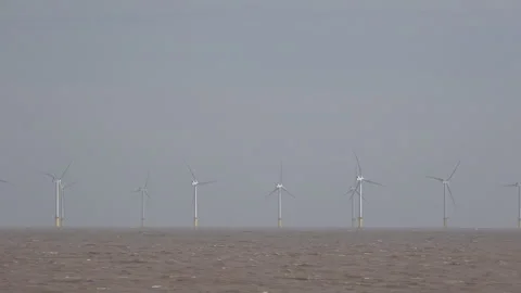 Off shore wind turbines with waves on beach England UK 4K Video stock 287764440