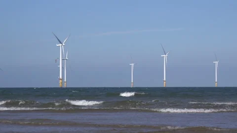 Off shore wind Turbines with waves in foreground and beach England UK 4K Video stock 206306466
