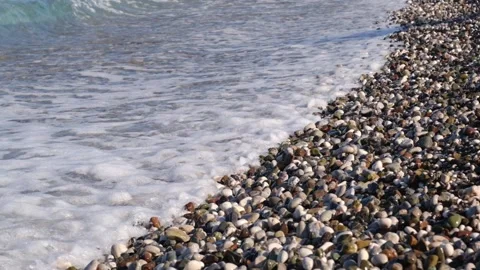 Shoreline with pebbles and shells as waves gently crash, creating ripples on 動画素材 346724146
