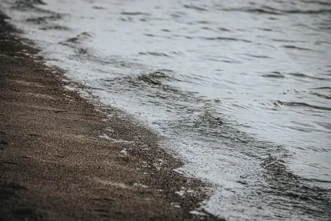 Shoreline view of gentle waves lapping against sandy beach with soft textur.. Stock Photos