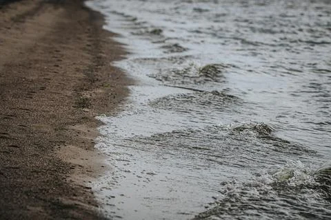 Shoreline view of gentle waves lapping against a sandy beach, with a natura.. Stock Photos