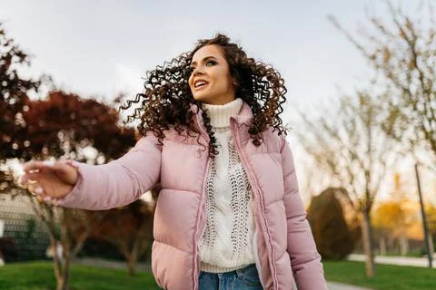 In a short down jacket in the park stands a girl reaching out her hand towards Stock Photos
