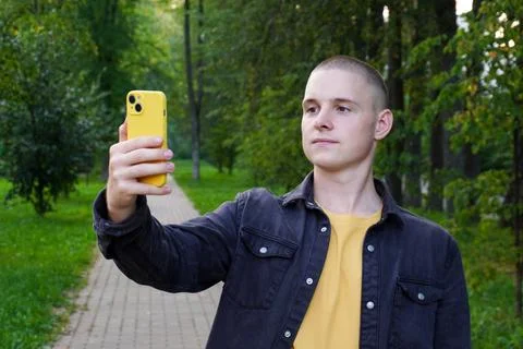 Short-haired athletic guy takes a selfie on a smartphone in a yellow case Stock Photos