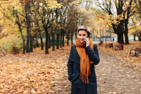 Short-haired blonde communicates on the phone walking in the autumn park in a Stock Photos